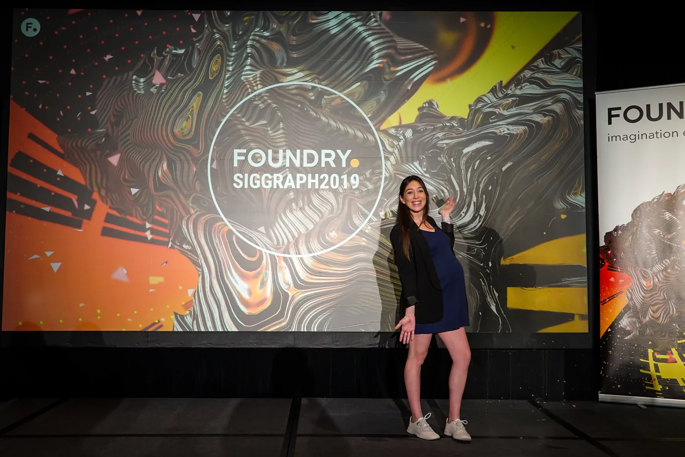 A speaker on stage in front of a colorful Foundry SIGGRAPH backdrop