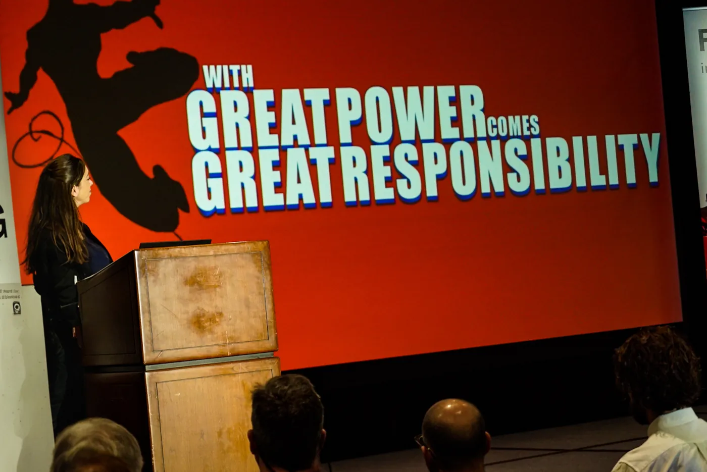 A speaker at the podium in front of a slide reading With great power comes great responsibility
